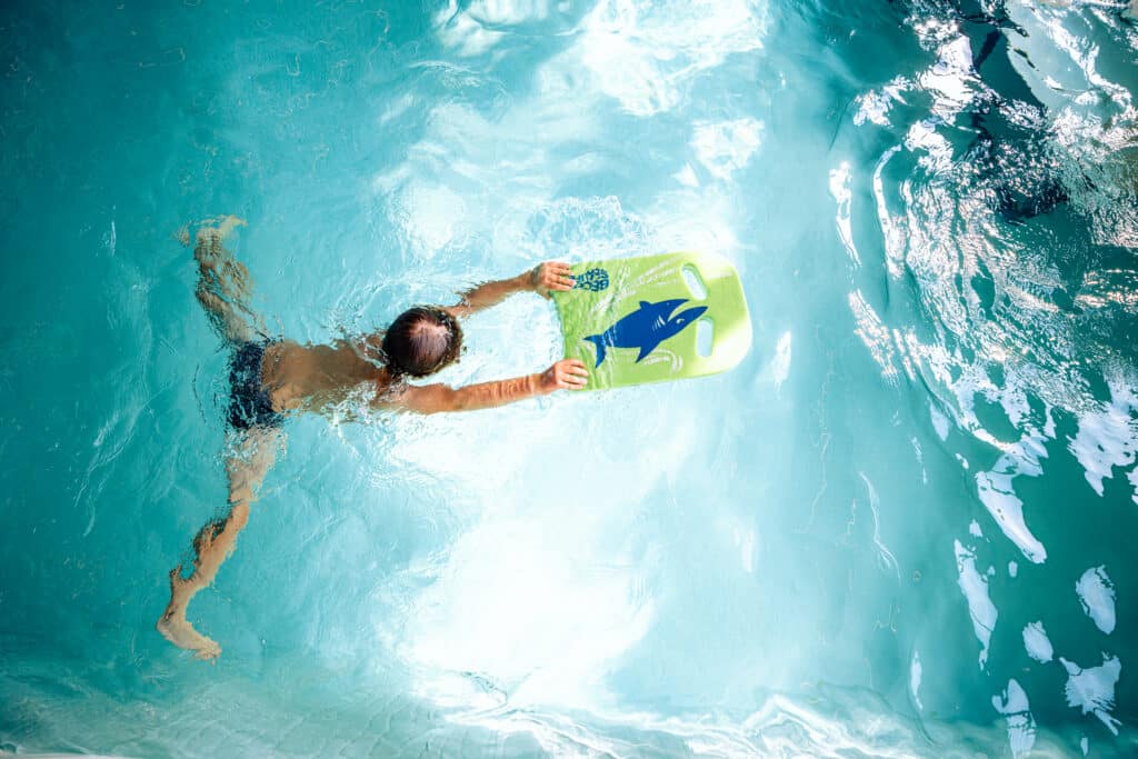 Kind oefent zwemmen met een kickboard tijdens een zwemles ter bevordering van waterveiligheid in Brussel.